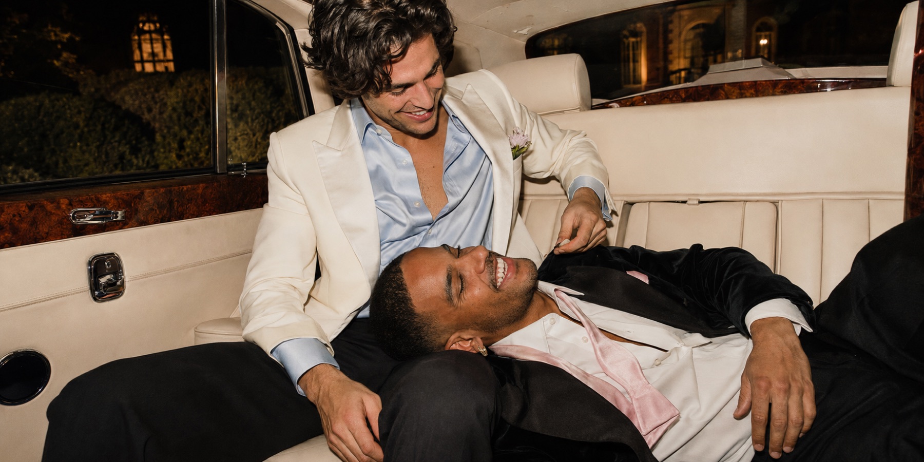 Two men laughing in the back of a vintage car at night